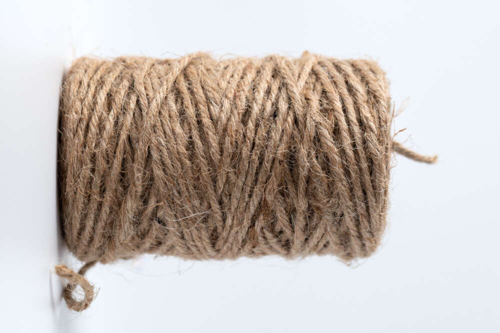 A tightly wound spool of natural jute fiber with a rough texture against a white background.
